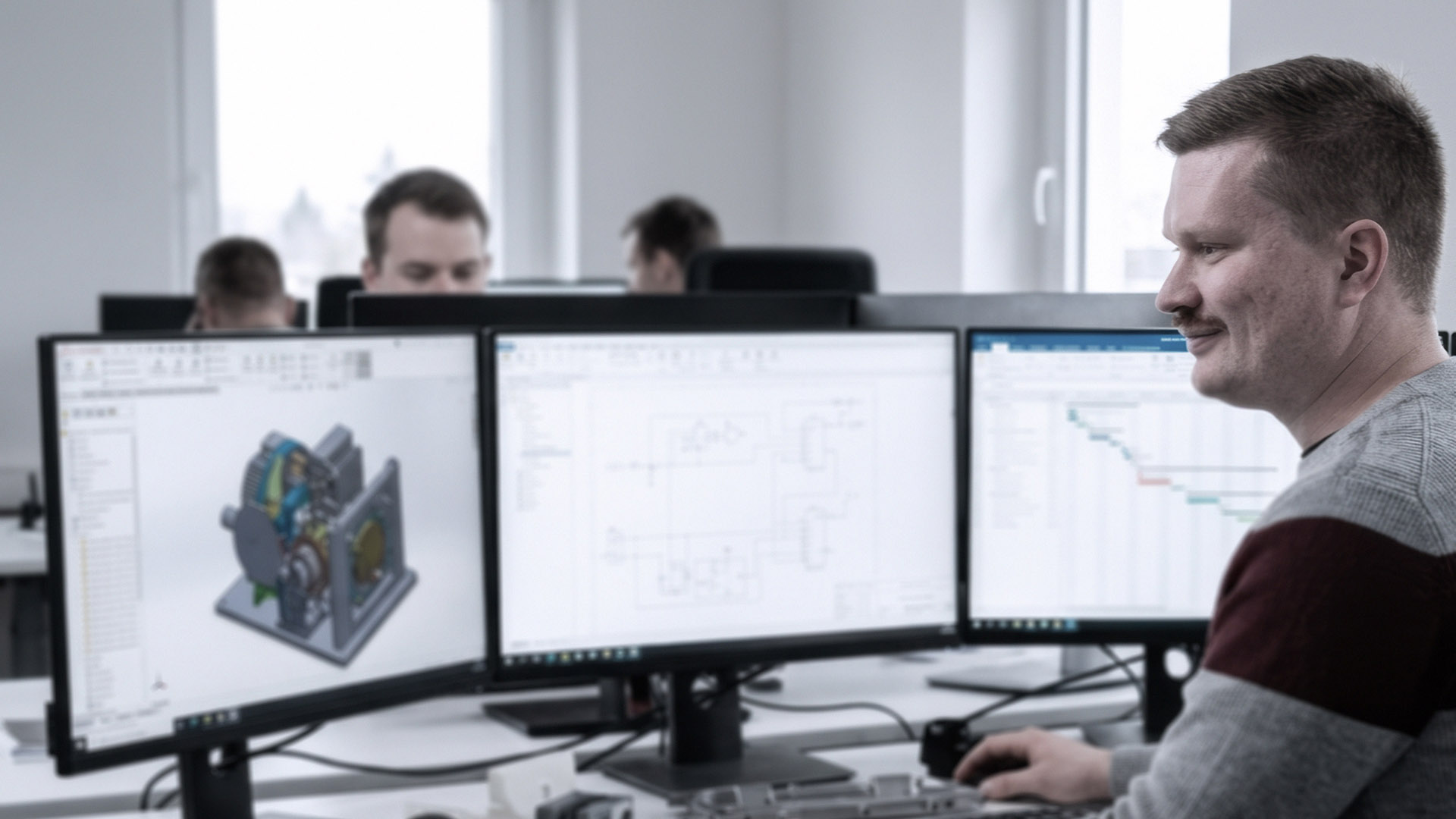 Dubbele schermen met CAD-omgeving in kantoor met engineers op achtergrond