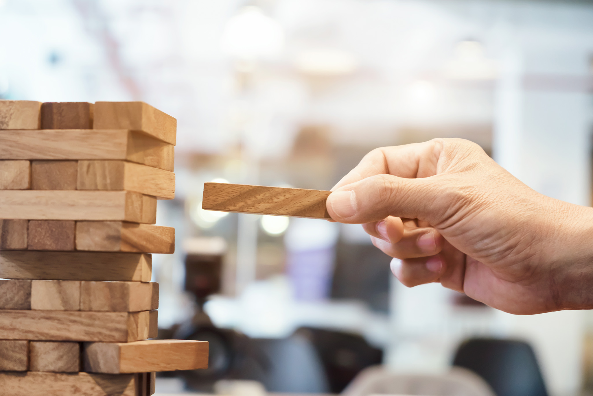 hand verwijdert blok uit houten toren als metafoor voor gestructureerde aanpak en risicobeheersing in engineering